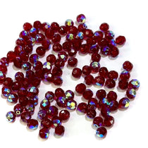 A pile of round, faceted, red glass beads with aurora borealis coating, used for jewelry making.