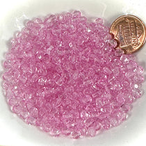 Pink glass beads on a white plate with a penny for scale