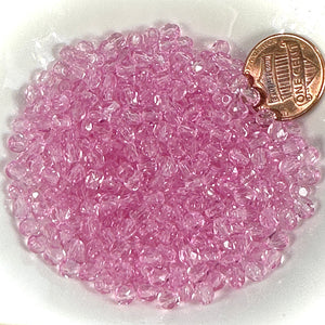 Pink glass beads on a white plate with a penny for scale