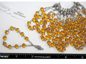 A finger auto rosary chain with centerpiece, featuring 6mm light topaz AB coated glass druk beads and silver-plated components, displayed alongside a ruler for scale.